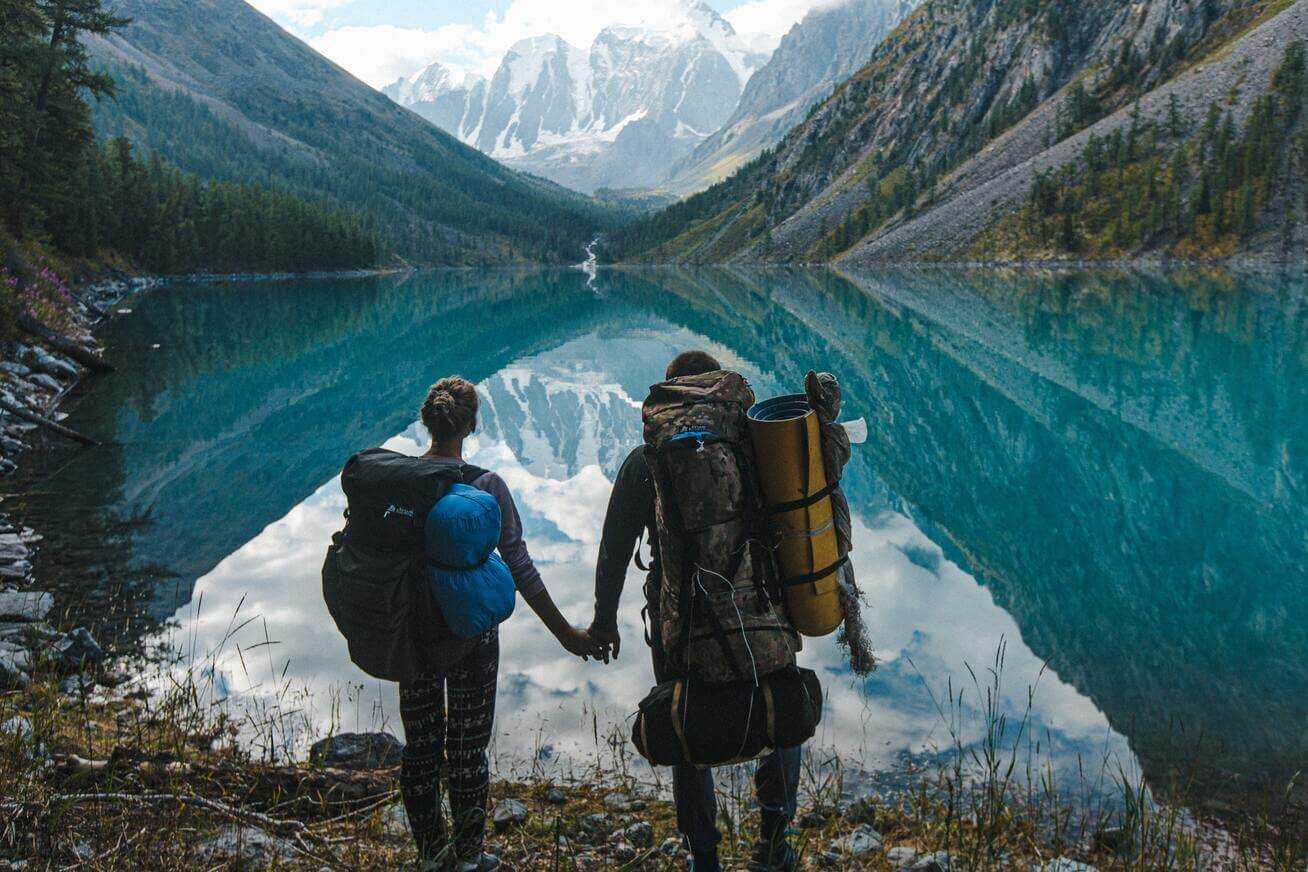 Two backpackers in front of a crystal clear lake in the midst of the mountains